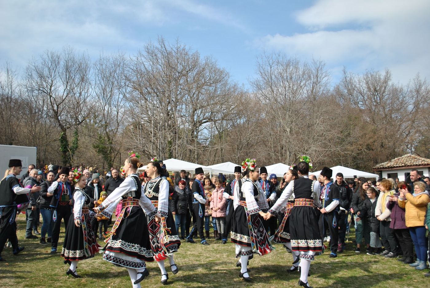 Un grupo de bailarines con trajes tradicionales danza en corro sobre la hierba ante una multitud de espectadores.