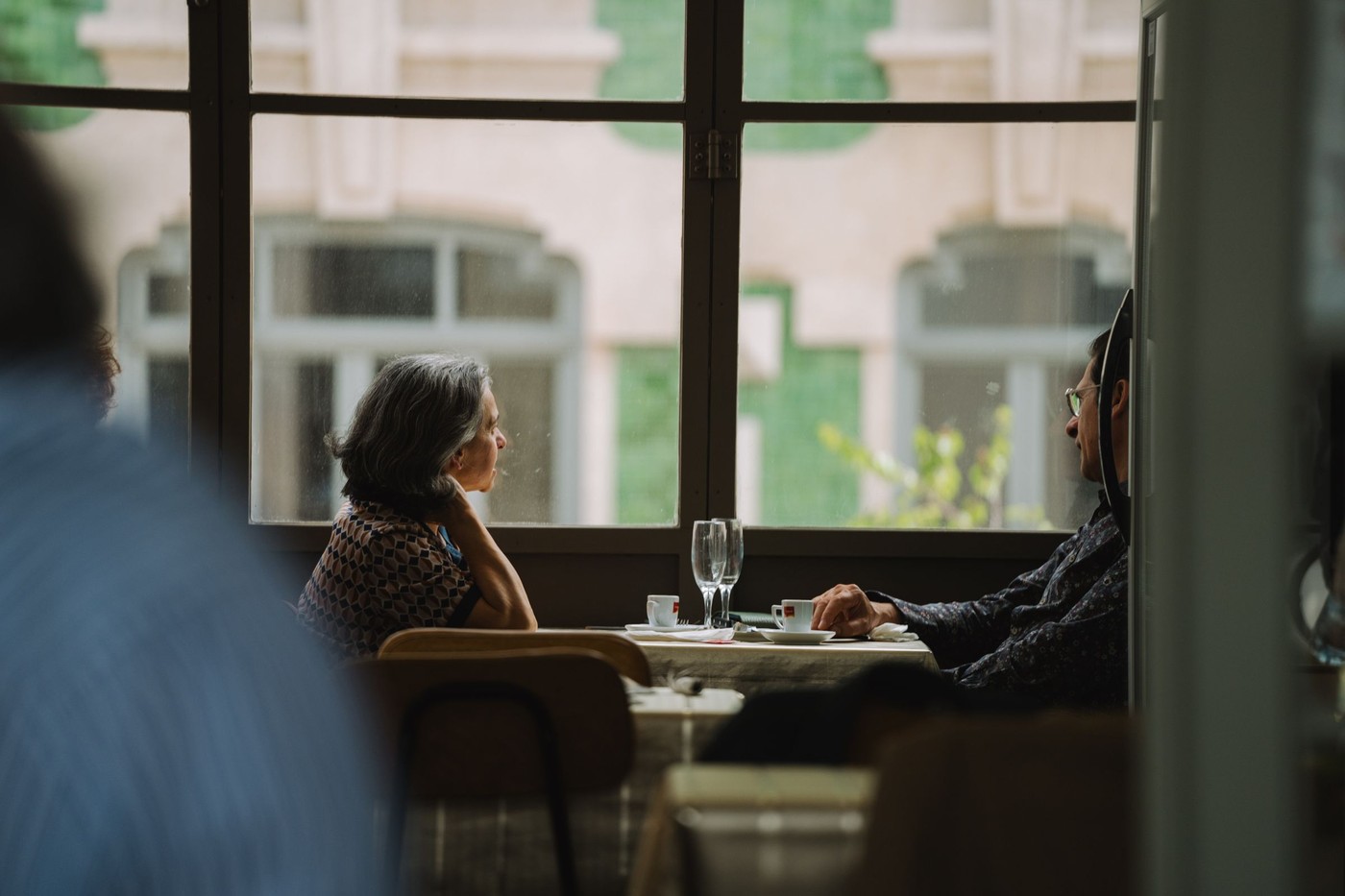 Pareja anciana sentada junto a la ventana, disfrutando de café en un acogedor café.
