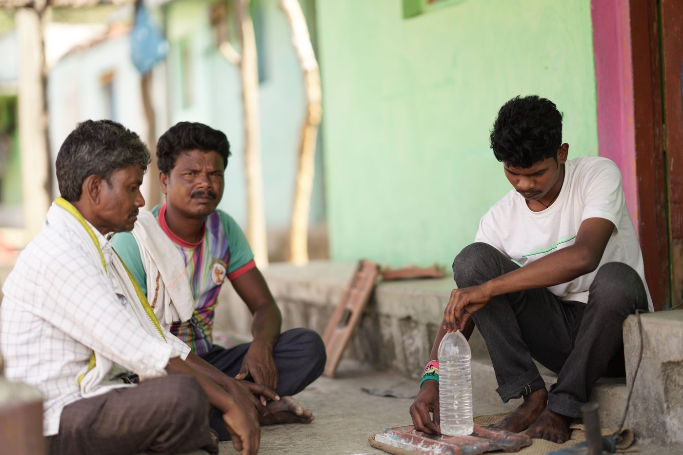 Tres hombres están sentados afuera en una aldea colorida, conversando.