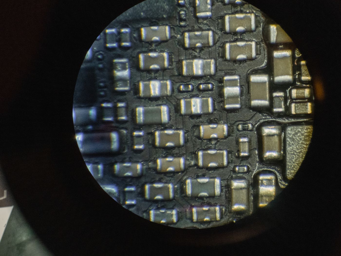Vista de microscopio de componentes electrónicos minúsculos montados sobre una placa de circuito, con las pistas y la soldadura a la vista.