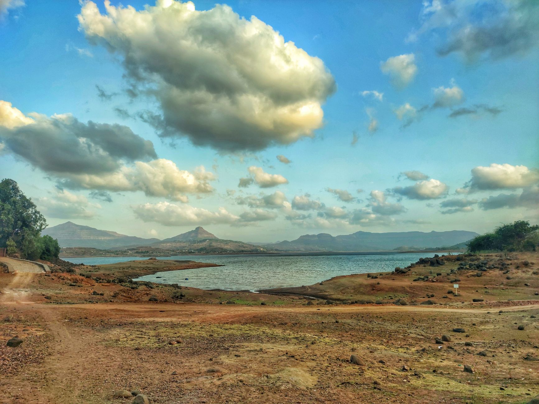 Lago tranquilo rodeado de montañas con nubes sobre un cielo azul, ejemplo de hidrosfera y atmósfera