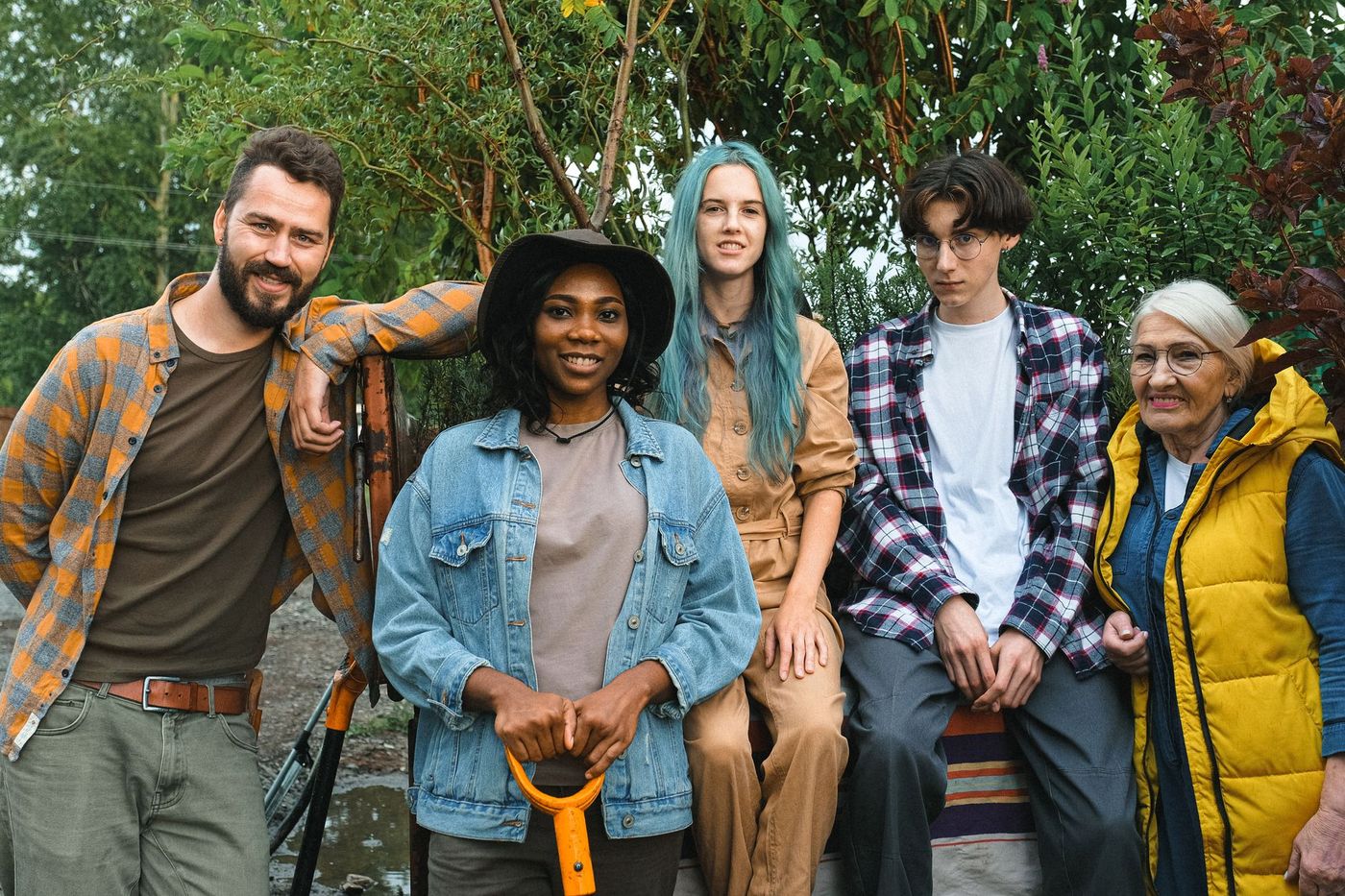 Grupo intergeneracional de cinco personas posa al aire libre entre vegetación, con ropa casual y herramientas de jardinería de mango naranja.