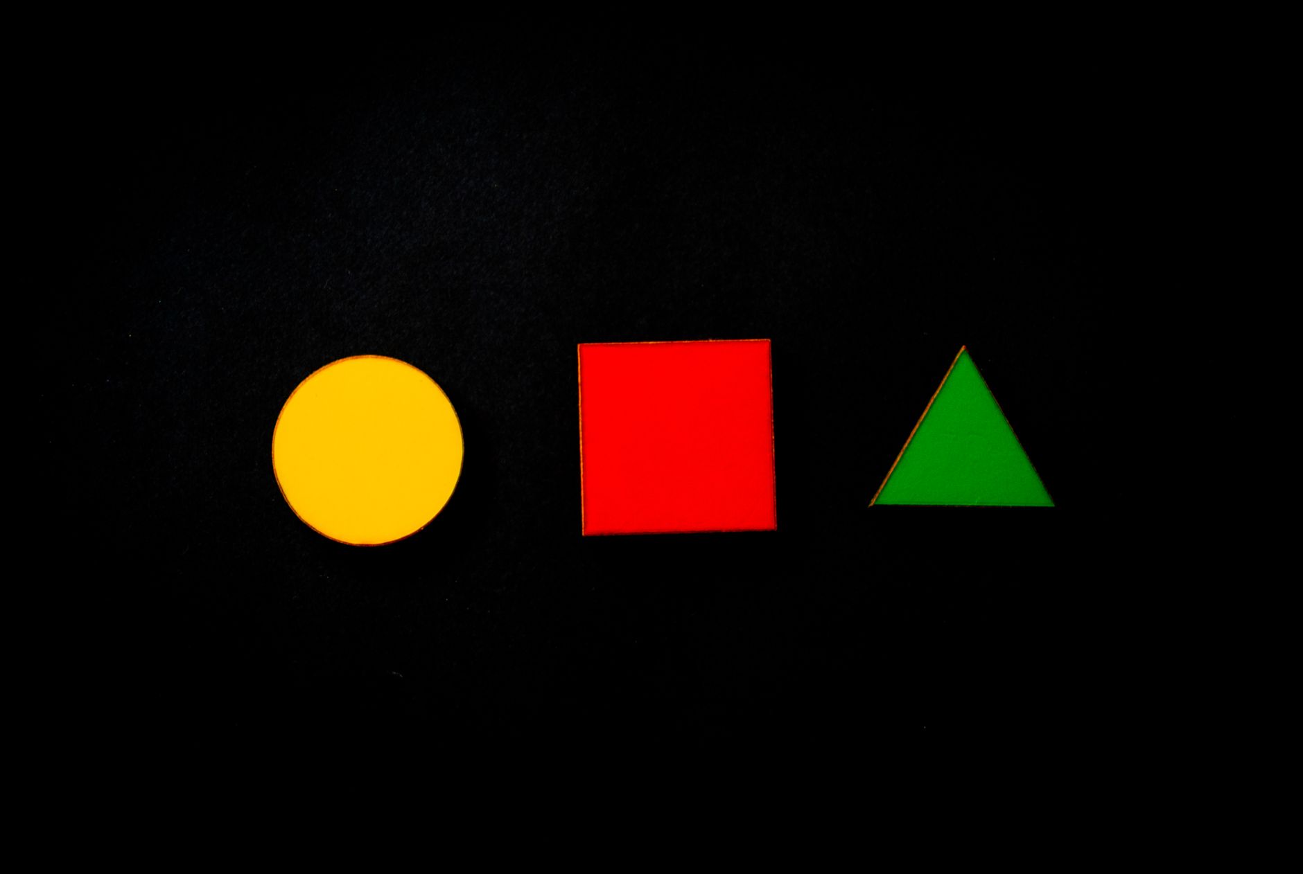 Círculo amarillo, cuadrado rojo y triángulo verde alineados sobre fondo negro