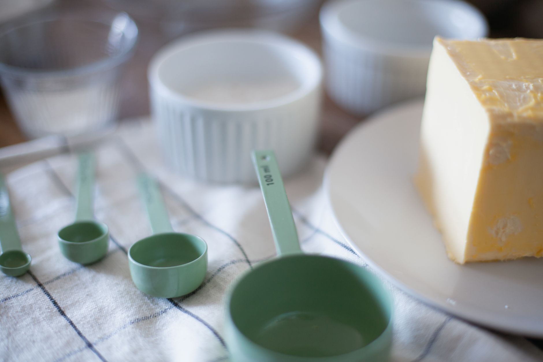 Tazas y cucharas medidoras verdes junto a mantequilla sobre una superficie de mármol