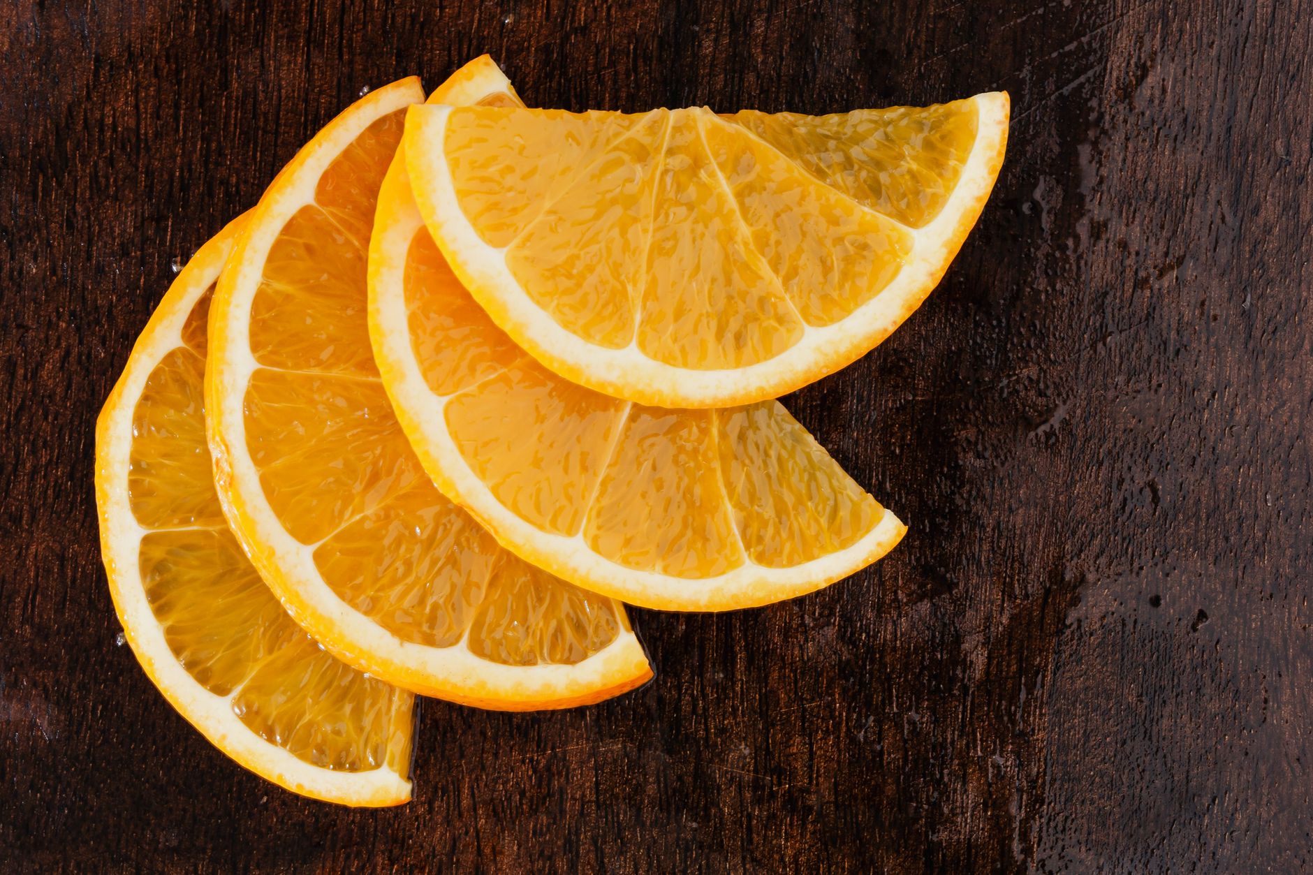 Rodajas de naranja cortadas sobre una superficie de madera oscura