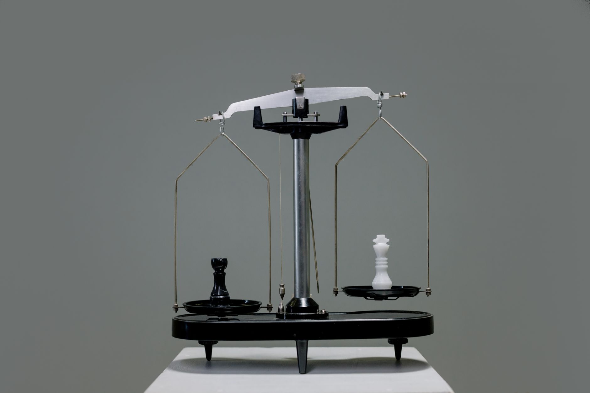 Balanza de dos platillos con piezas de ajedrez equilibradas sobre un fondo gris liso