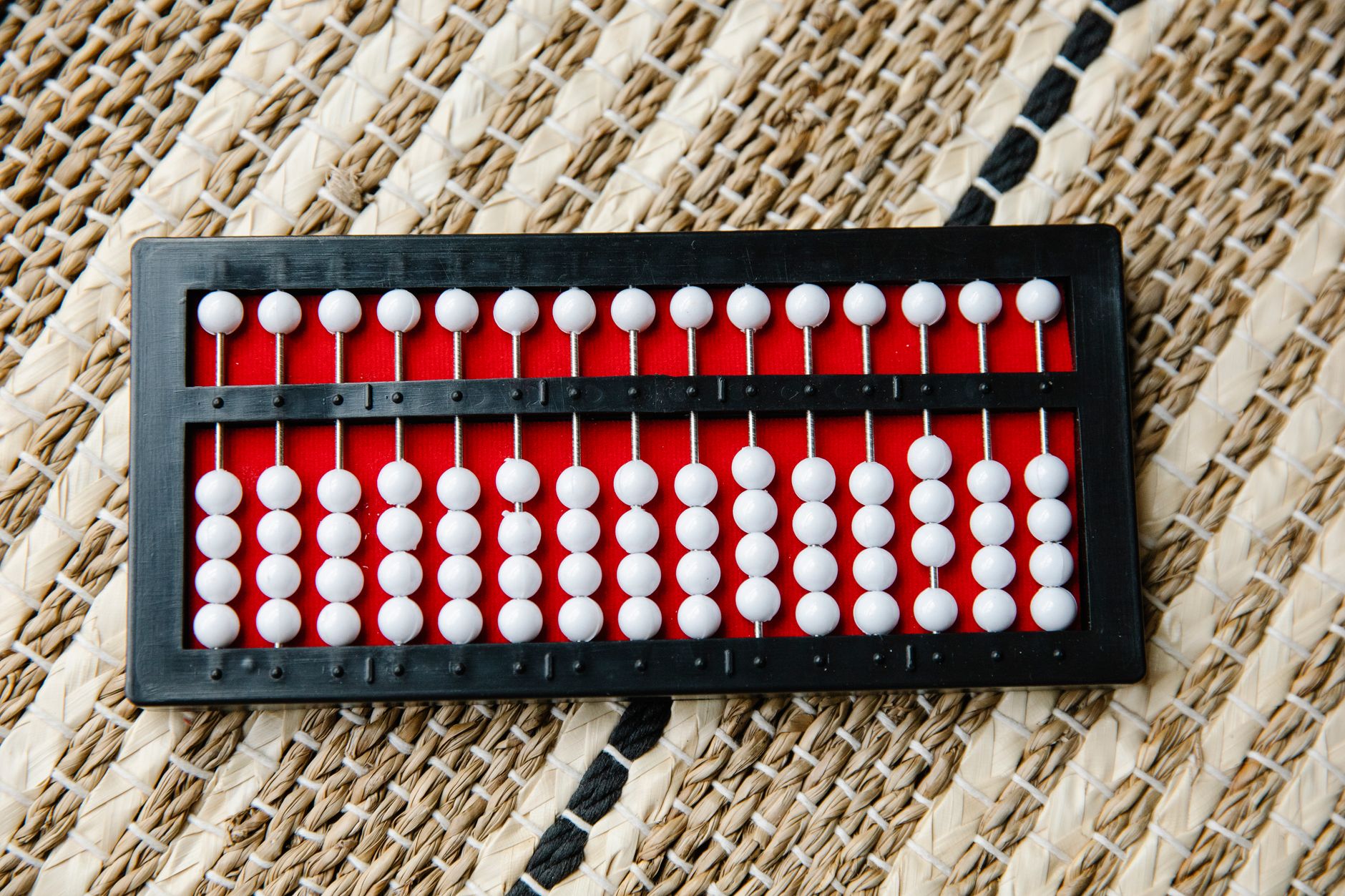 Ábaco tradicional con cuentas rojas y blancas sobre una superficie de tejido trenzado
