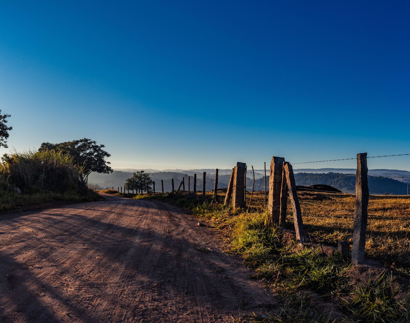 Una vista escénica de un camino de tierra y una cerca bajo un brillante cielo azul en el campo de Brasil.