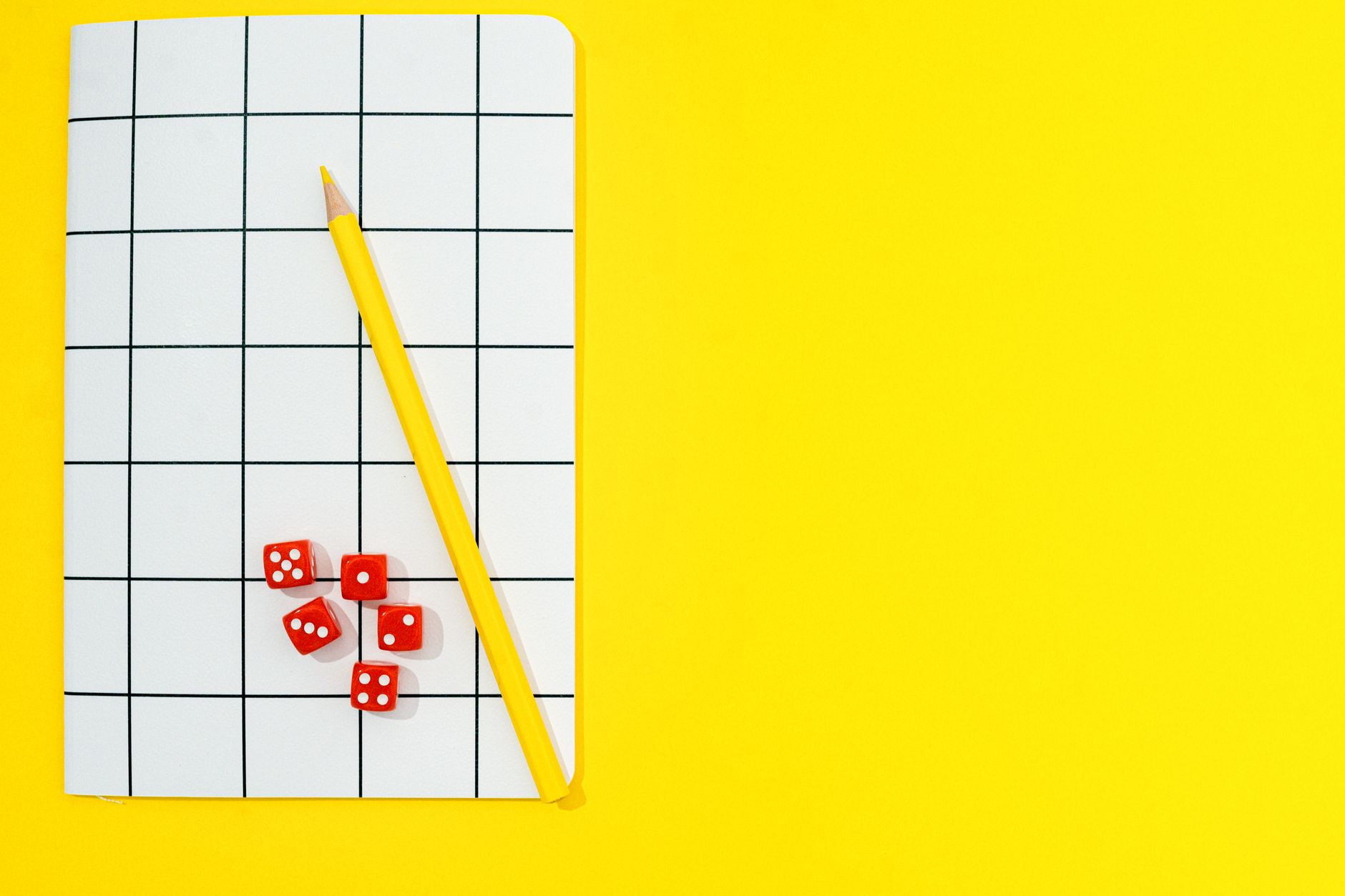 Papel cuadriculado, un lápiz de madera y dados rojos sobre un fondo amarillo