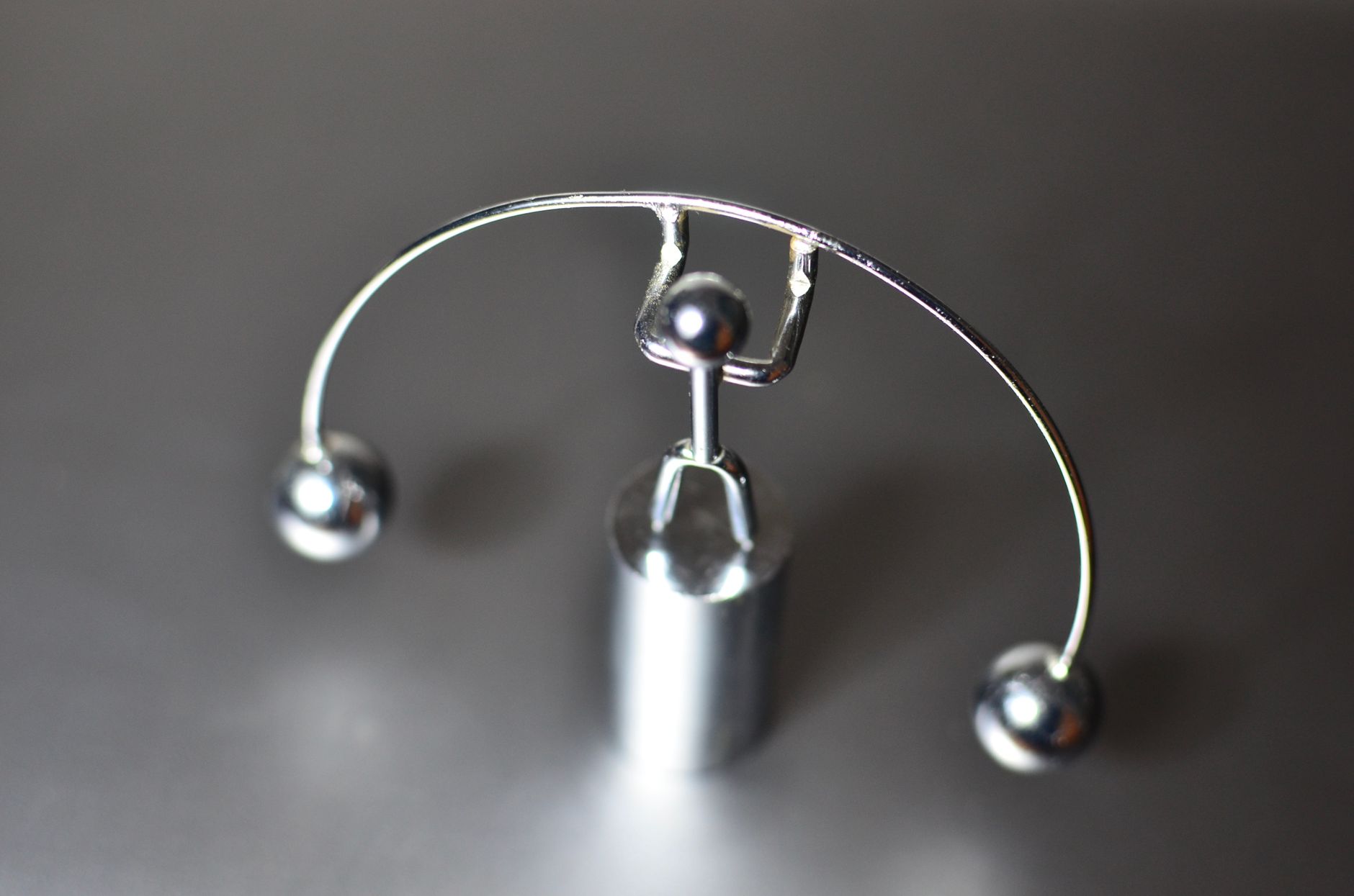 Escultura cinética de metal con dos esferas en equilibrio sobre una superficie gris