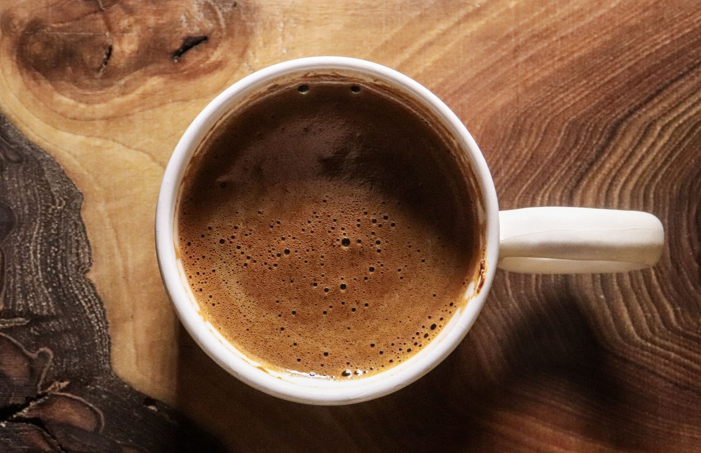 Vista superior de un café recién hecho en una taza blanca sobre una superficie de mesa de madera.
