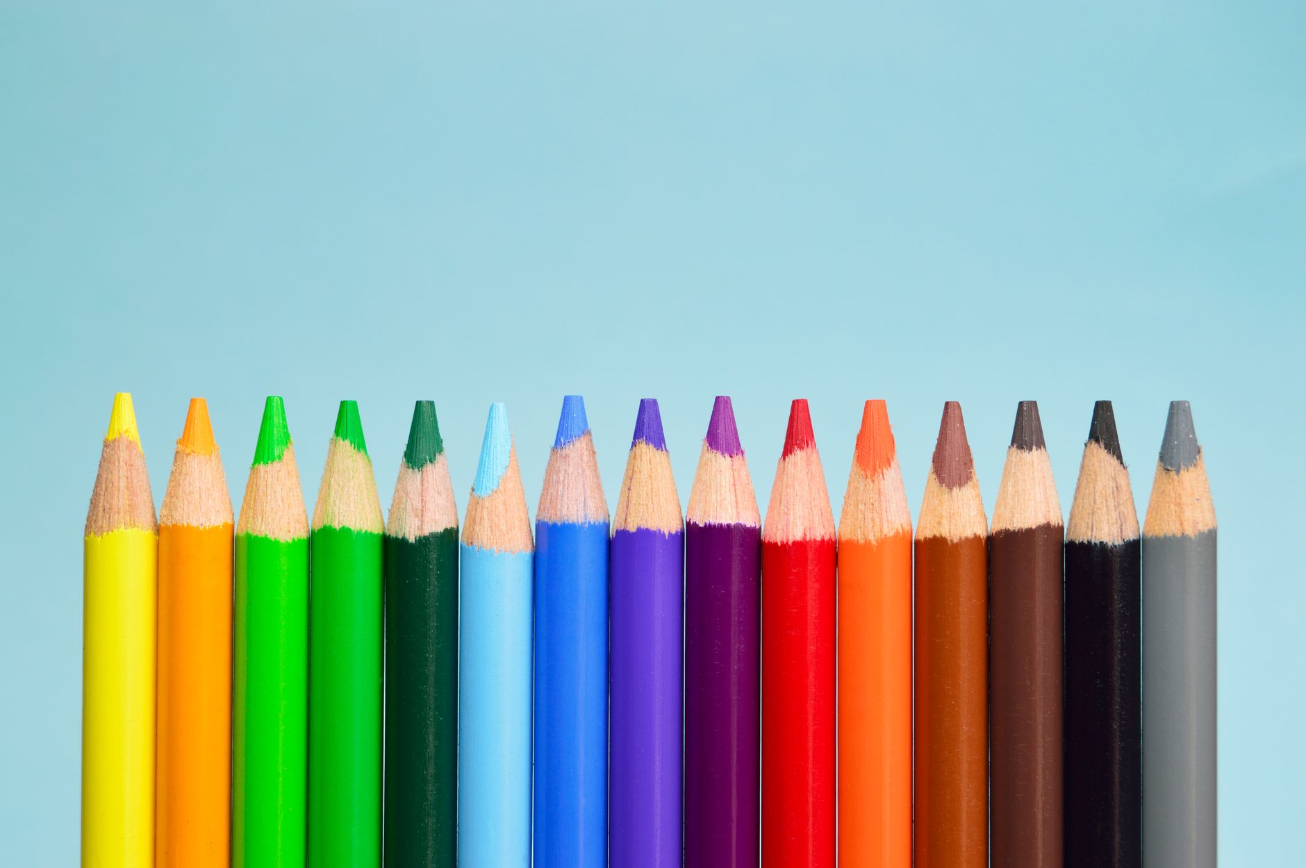 Fila de lápices de colores con las puntas hacia arriba sobre un fondo azul claro