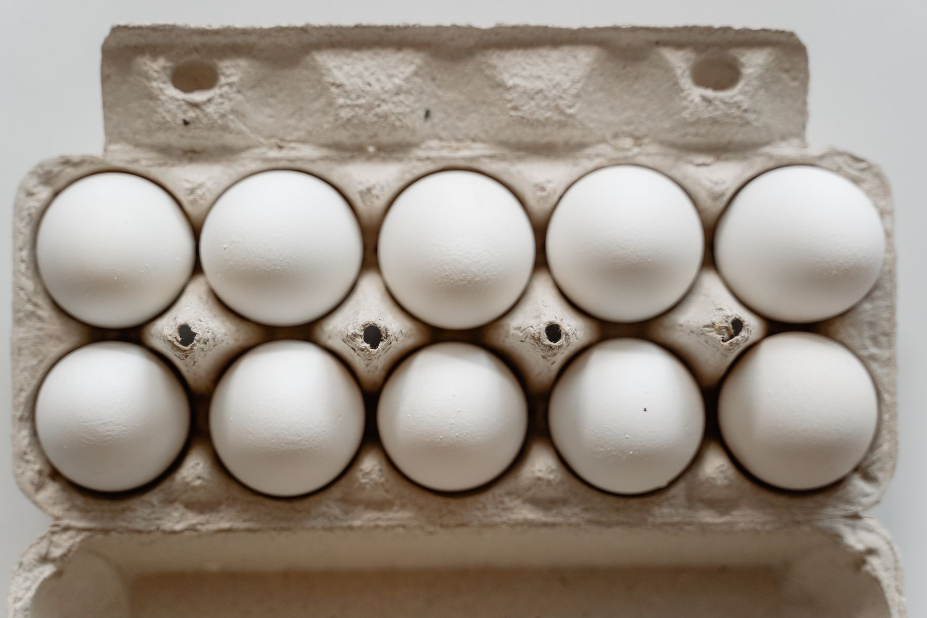Huevera de cartón abierta con diez huevos blancos ordenados, vista desde arriba