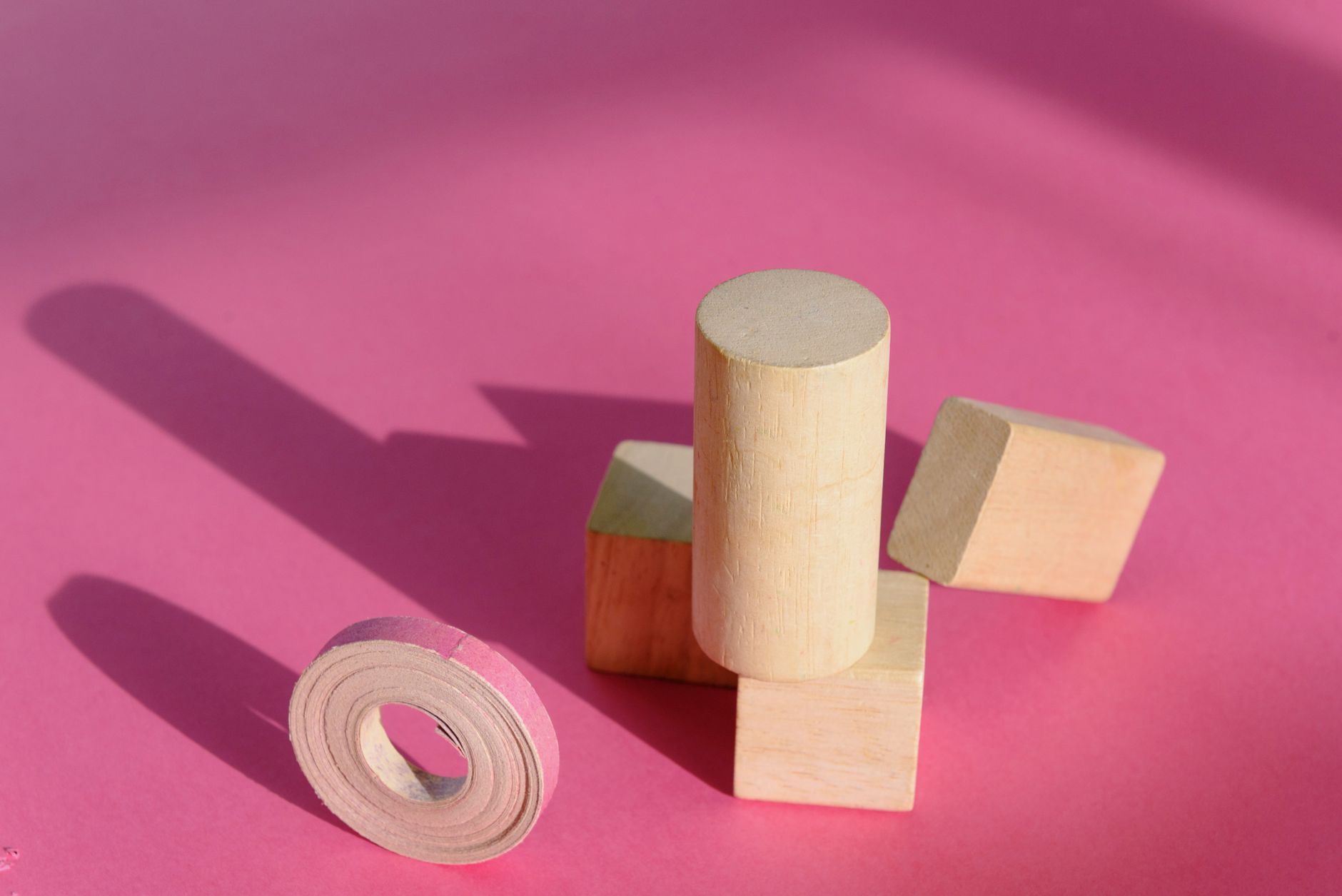 Cilindro, cubo y prismas rectangulares de madera sobre fondo rosa