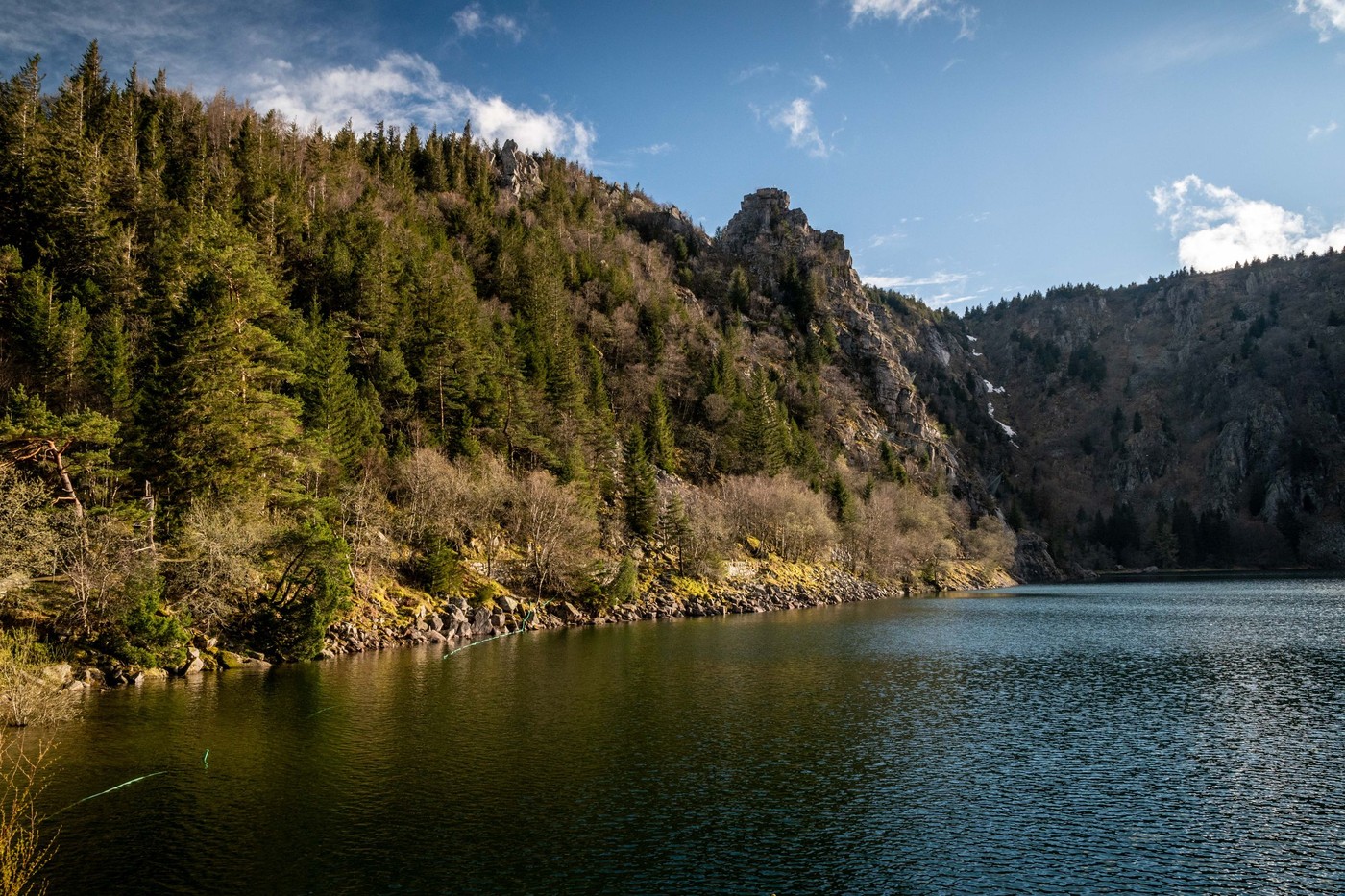 Un lago tranquilo rodeado de colinas rocosas y densos bosques de coníferas a la luz del día.