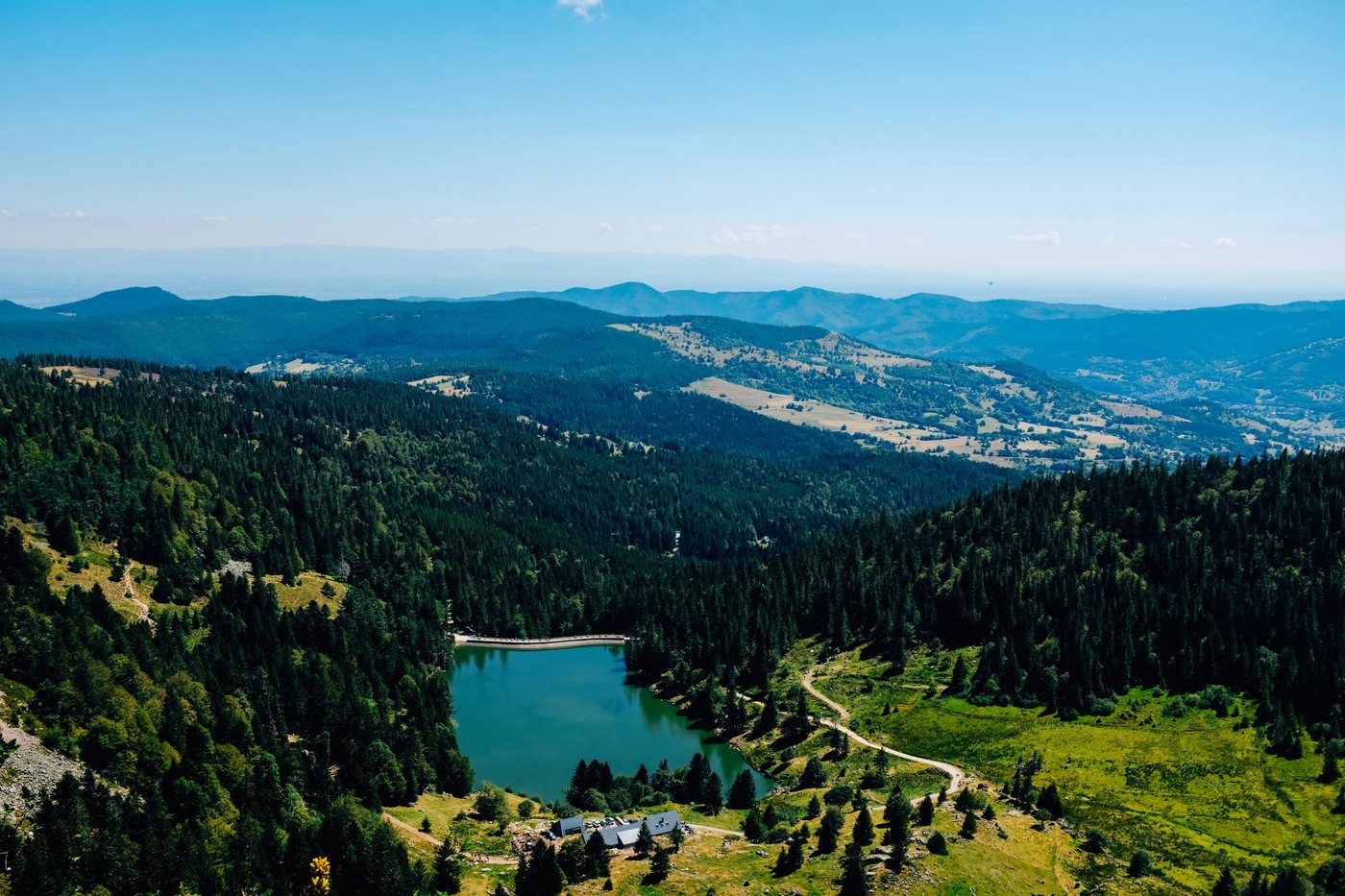 Increíble vista aérea de un paisaje montañoso verde con un lago sereno rodeado de bosques y colinas.