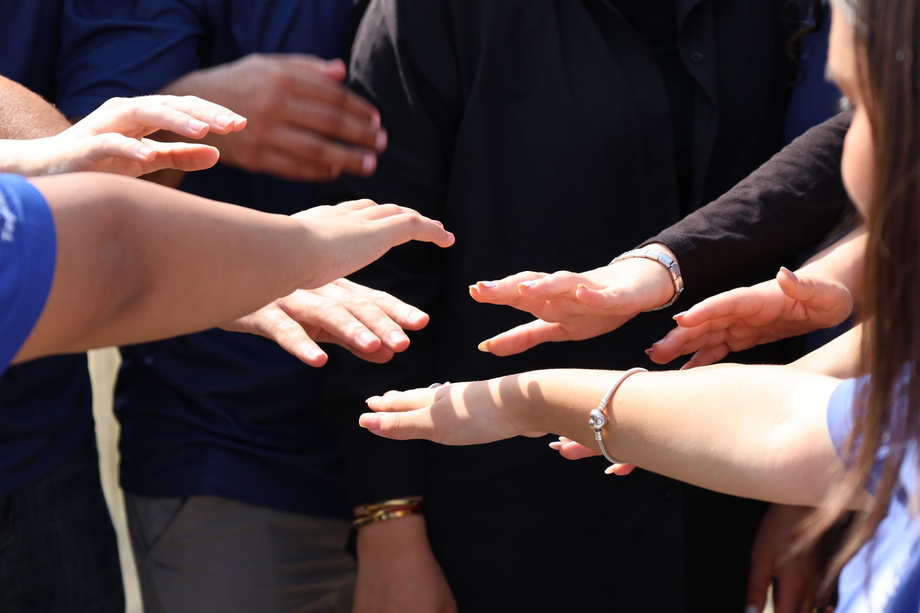 Varias personas con las manos extendidas hacia el centro de un círculo, en un gesto de unión y colaboración.
