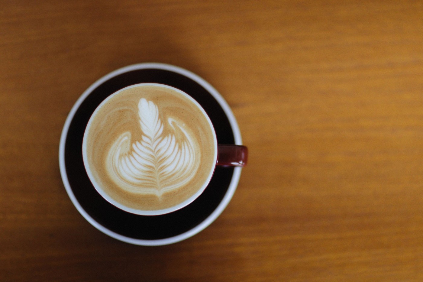 Un cappuccino bellamente elaborado con intrincado arte en latte, visto desde arriba sobre una mesa de madera.