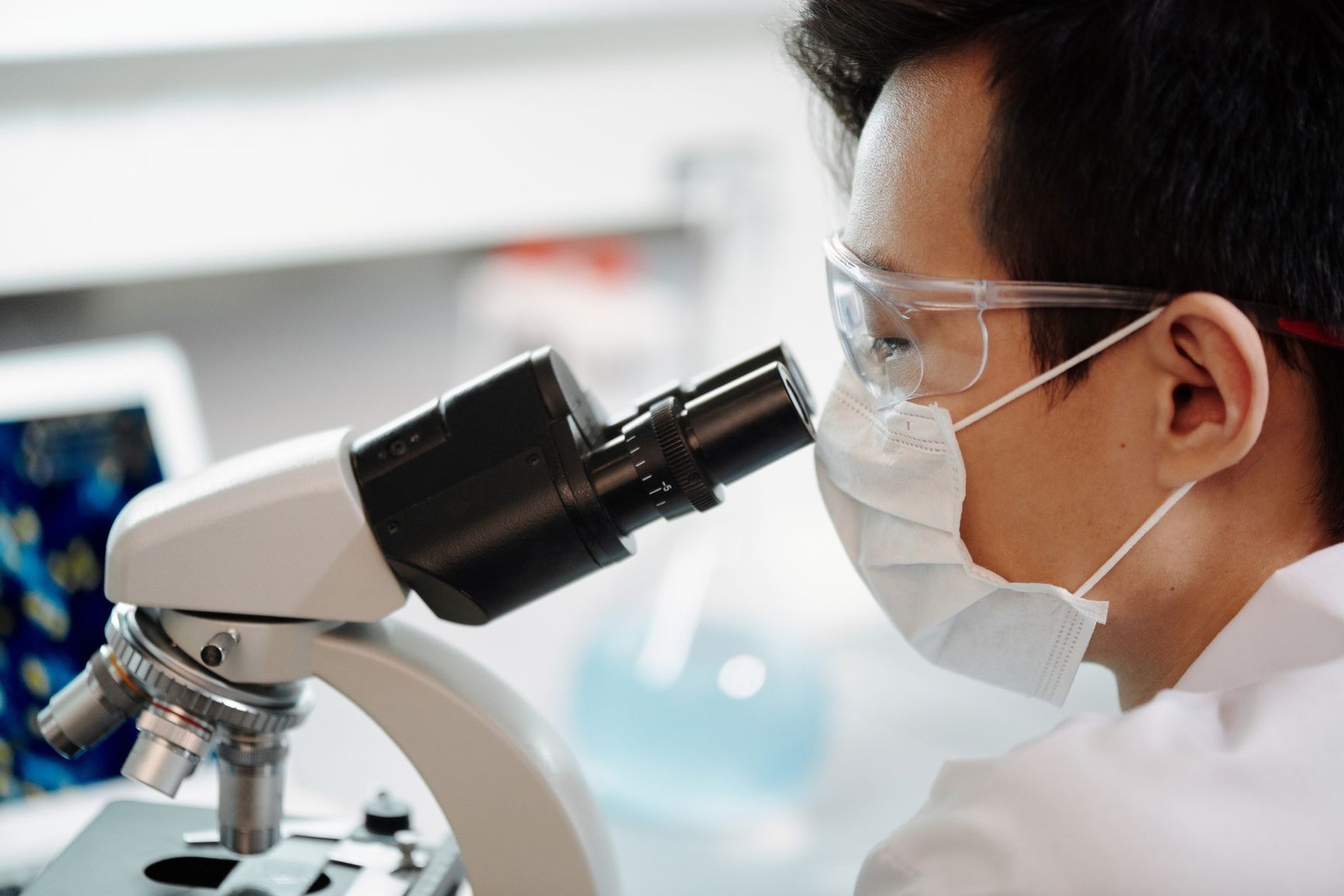 Investigador con mascarilla y gafas de seguridad mirando por el microscopio