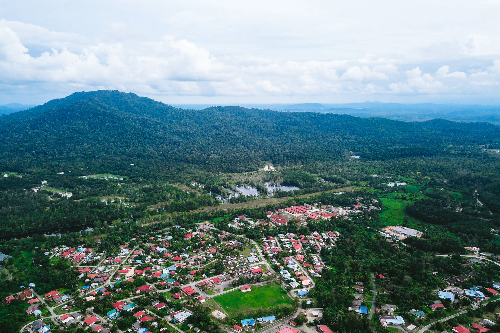 vista aérea de un poblado entre parcelas de cultivo y vegetación, con montañas al fondo