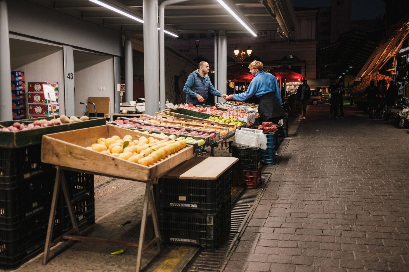 dos comerciantes adultos atienden su puesto de frutas y verduras dentro de un mercado de barrio