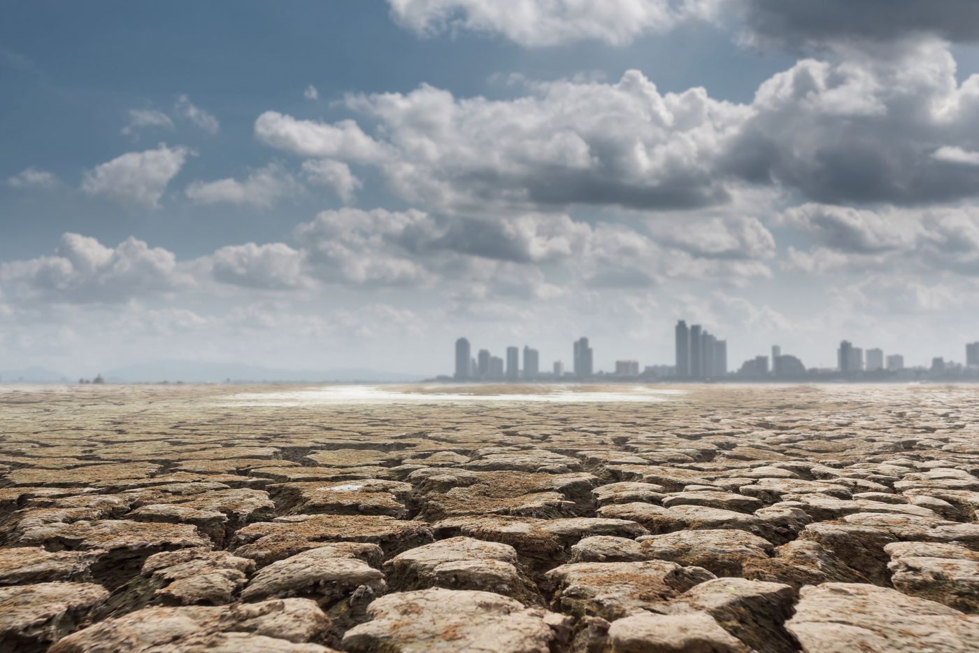 un terreno con la tierra agrietada por la sequía y, al fondo, el paisaje urbano
