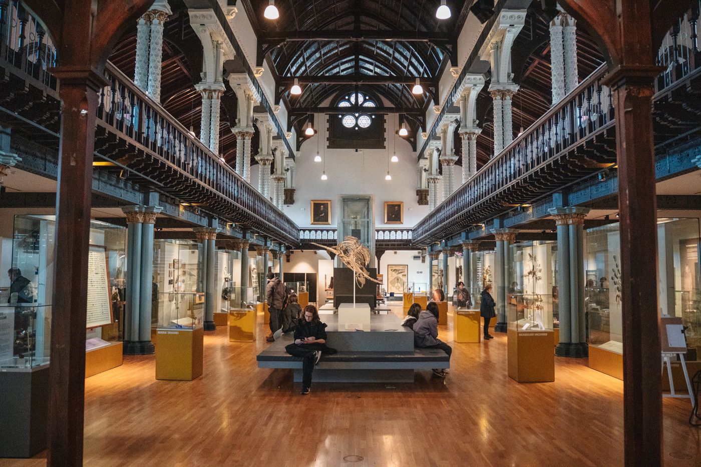 visitantes recorren una sala de museo con vitrinas y bancos