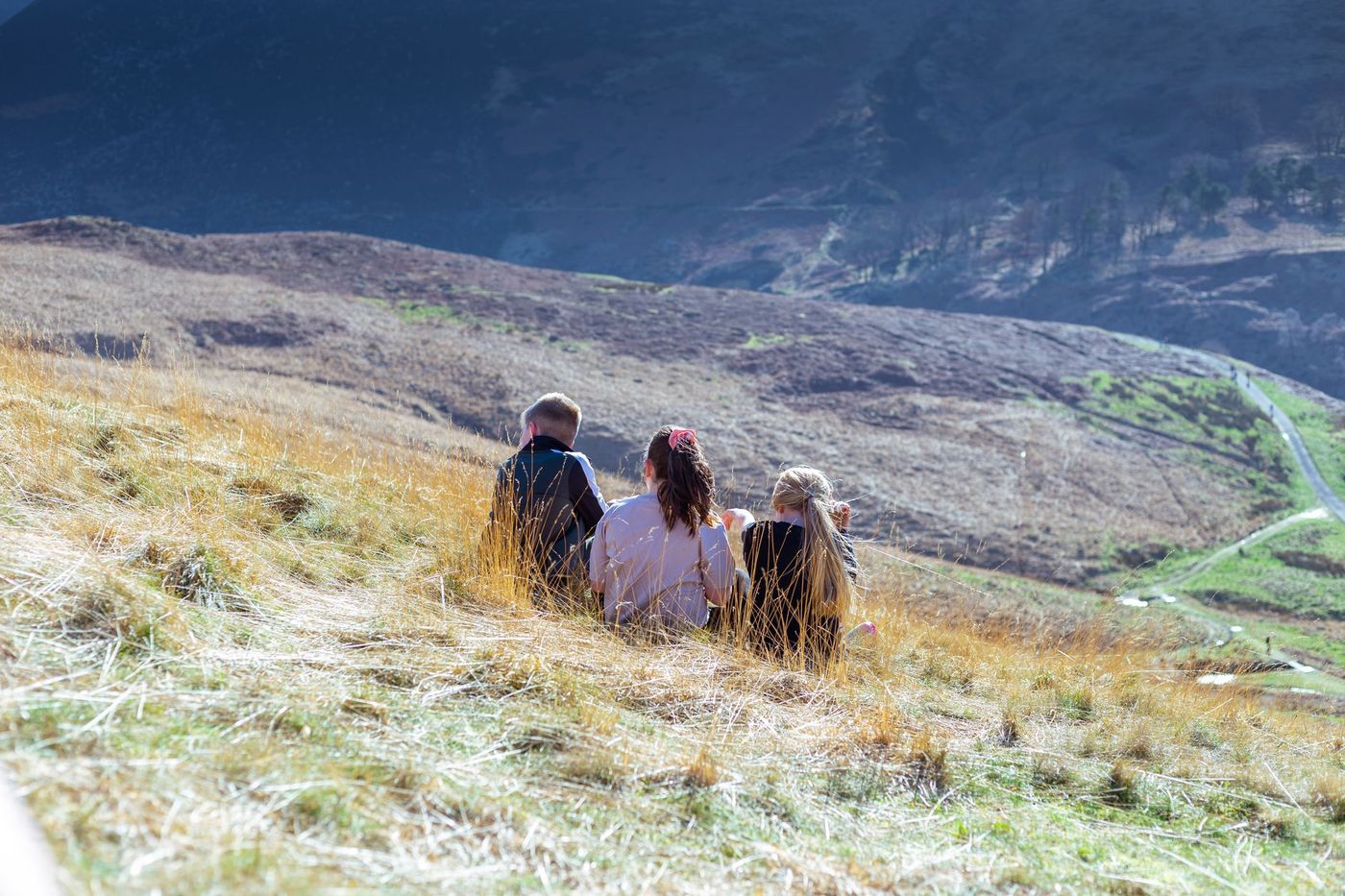 Tres estudiantes sentados en una loma observan el paisaje del entorno de su comunidad.