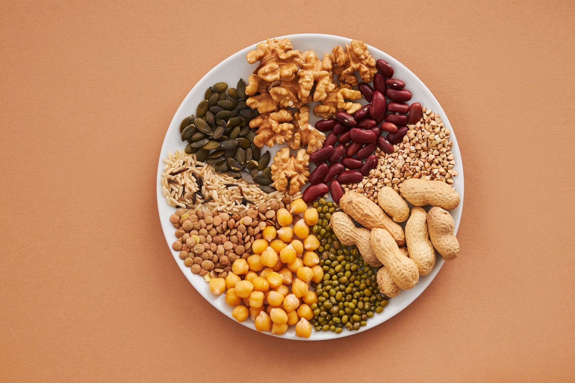 Frutos secos, semillas y legumbres repartidos en un plato blanco, vistos desde arriba.