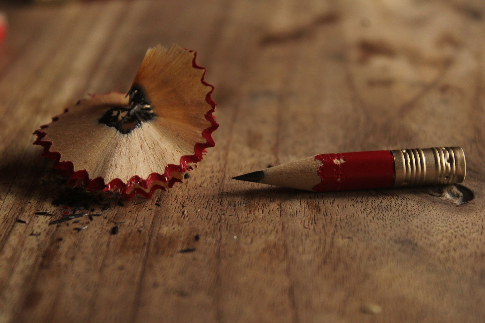 Lápiz rojo afilado junto a una viruta de madera sobre una mesa rústica