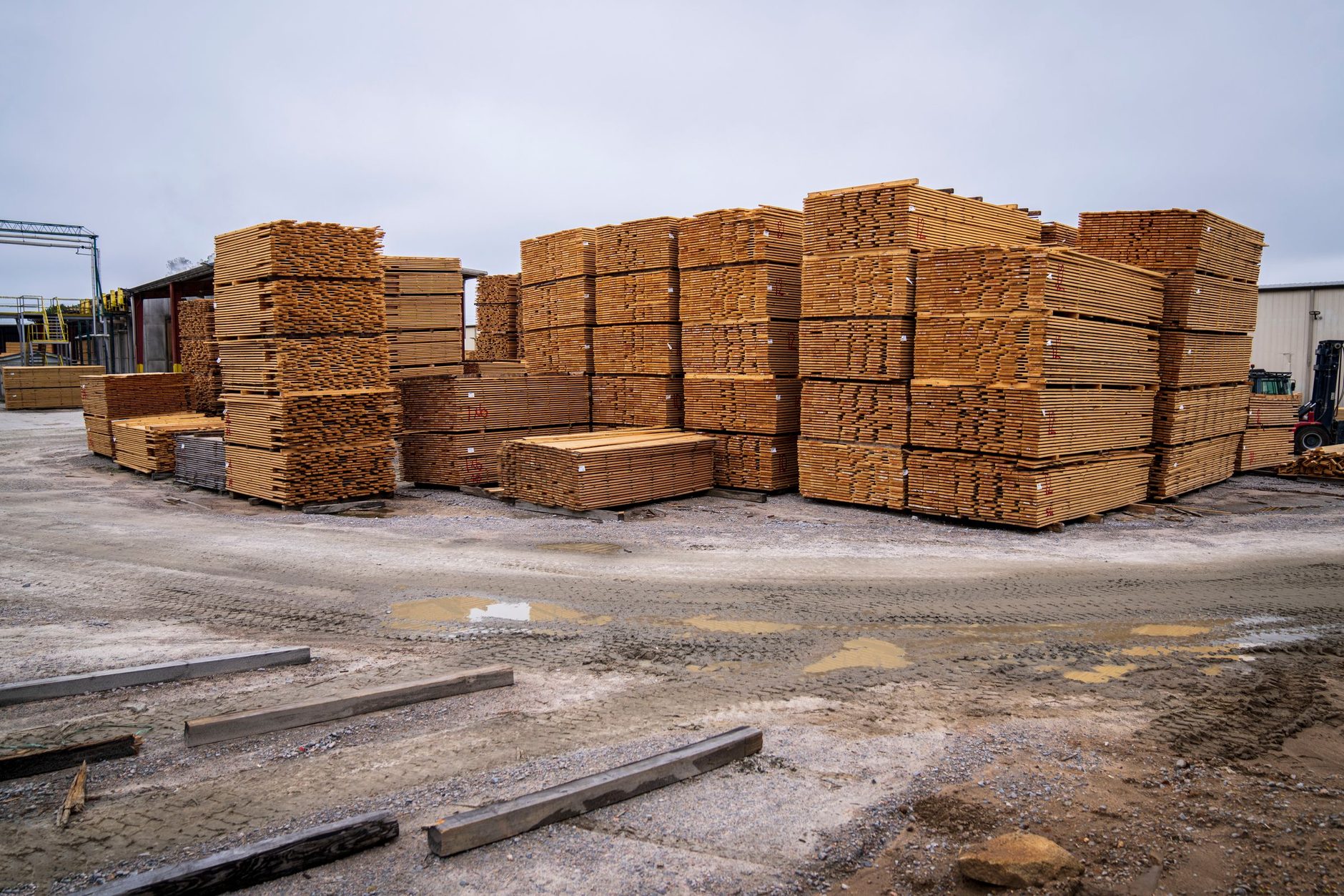 Pilas de tablas de madera ordenadas en un patio industrial al aire libre.