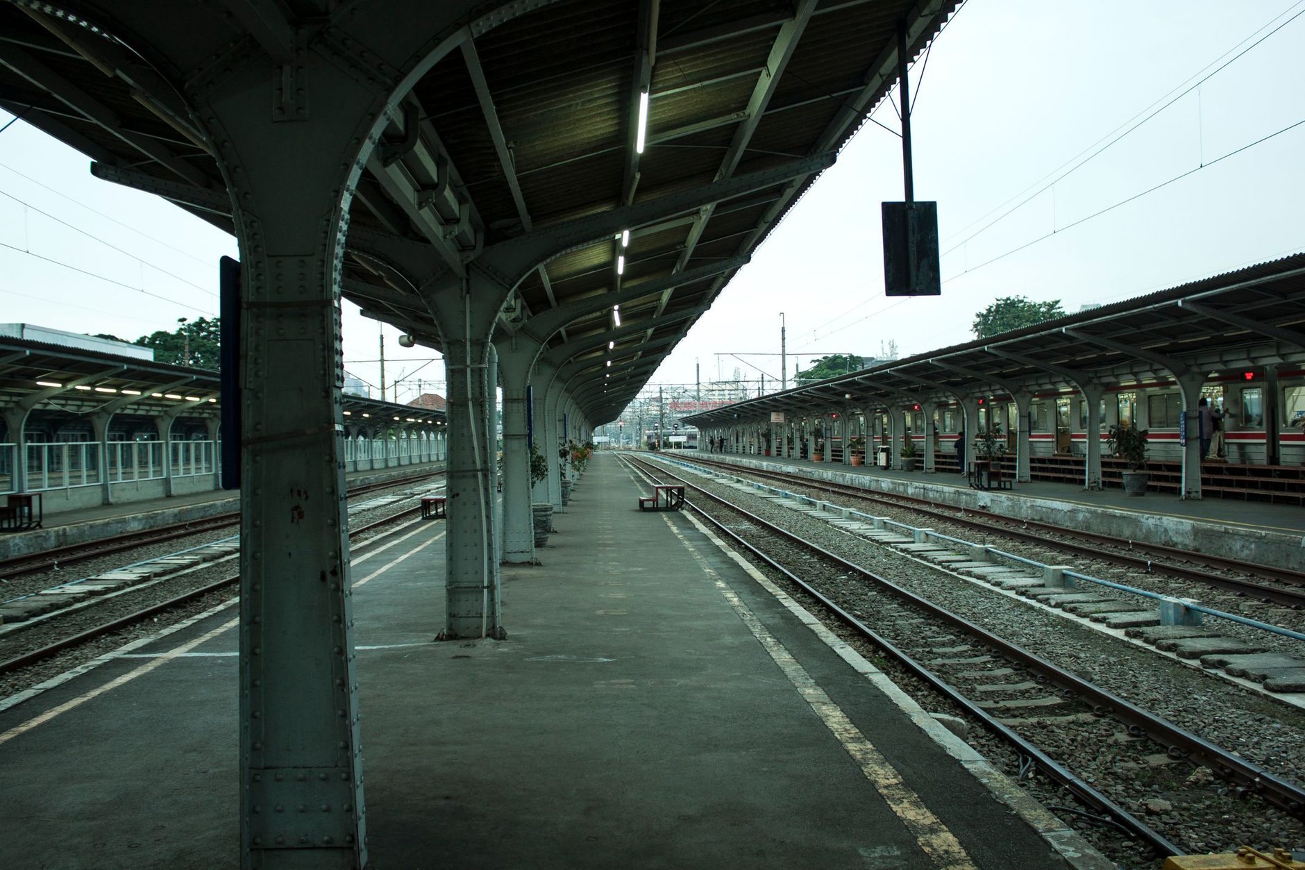 Andén de estación de tren vacío con varias vías y un tren detenido al fondo, bajo un cielo nublado
