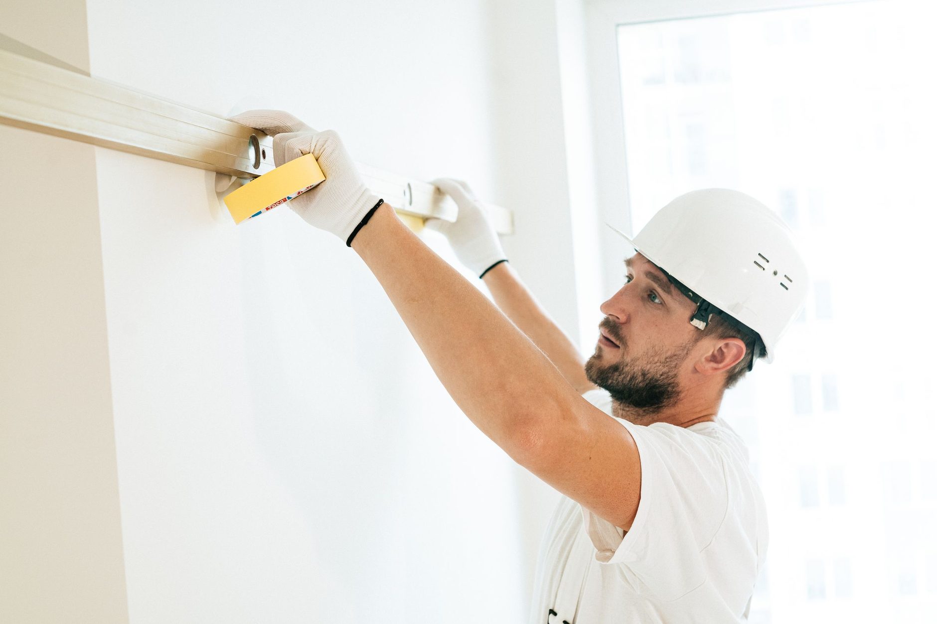 Un trabajador con casco mide con un flexómetro la longitud de un perfil fijado a la pared, en un interior luminoso.