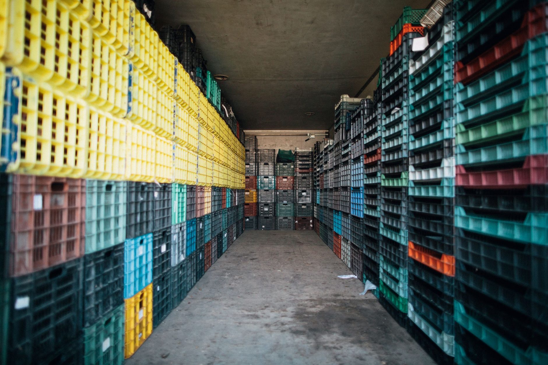 Pilas de cajas de plástico apiladas en hileras a ambos lados del pasillo de un almacén