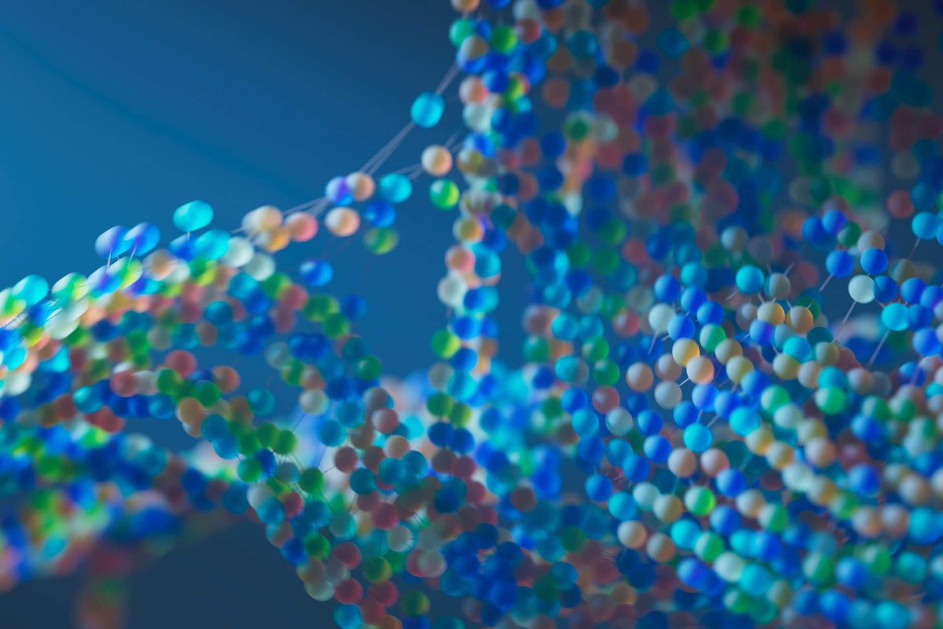 Recreación tridimensional de una doble hélice de ADN: dos cadenas de esferas de colores unidas por varillas claras, sobre fondo azul.