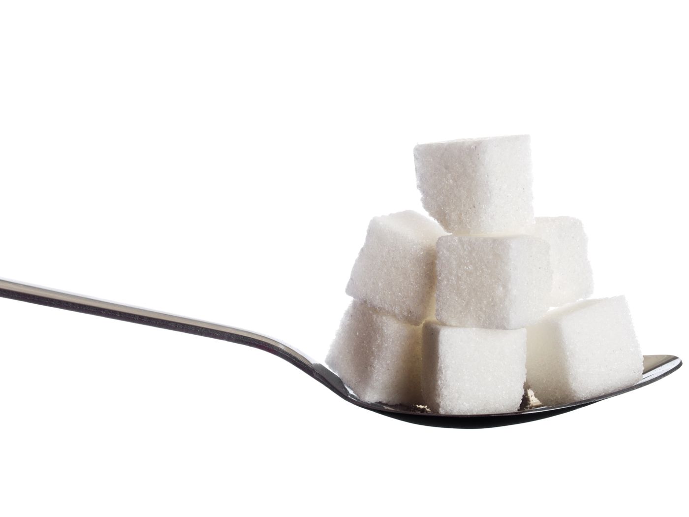 Terrones de azúcar blanco apilados sobre una cuchara metálica, aislados sobre fondo blanco.