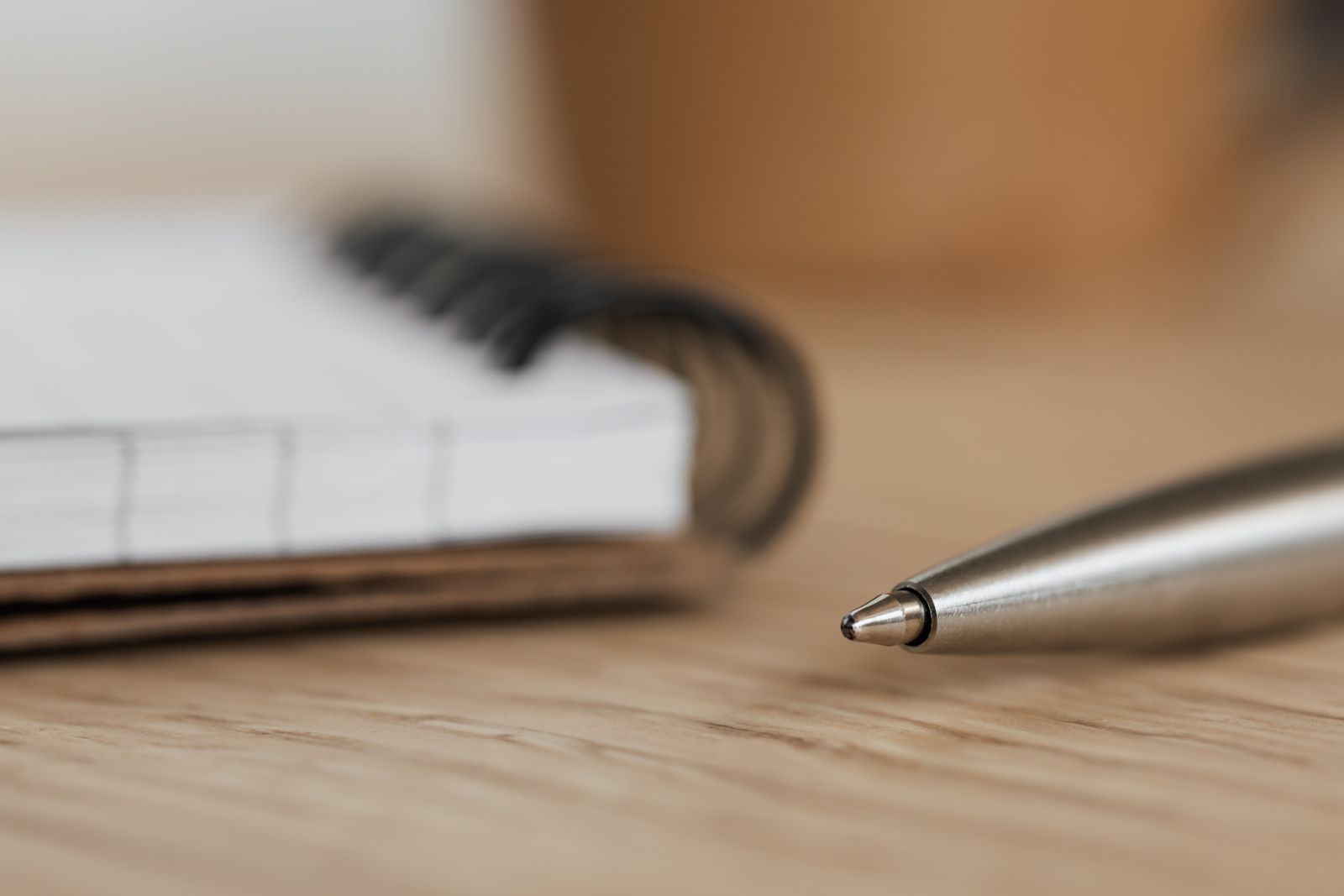 Cuaderno abierto de páginas en blanco junto a un bolígrafo metálico sobre una mesa de madera