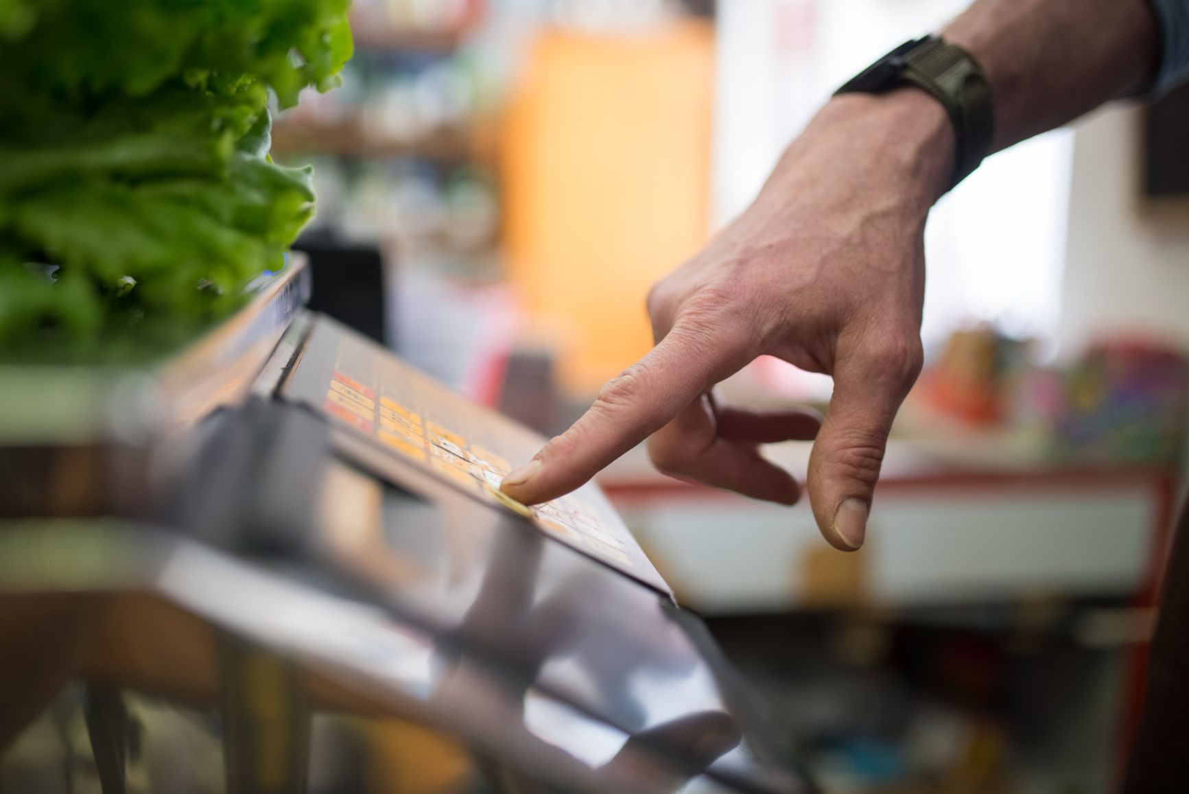 Una mano usando una balanza digital en la sección de productos al peso