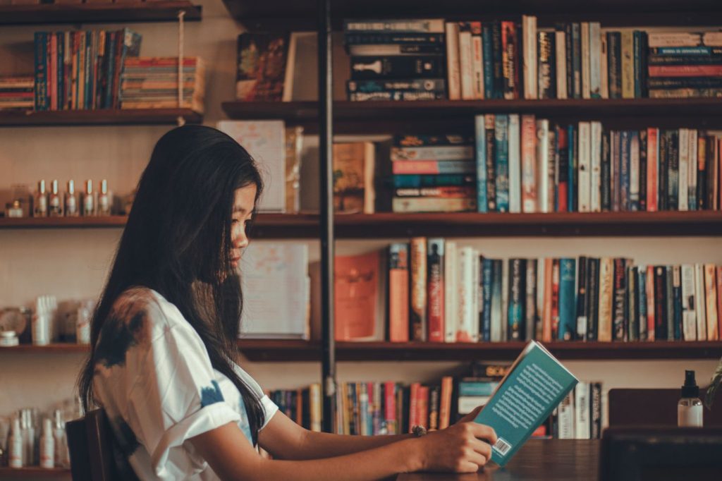 Persona adulta leyendo un libro entre estanterías de biblioteca