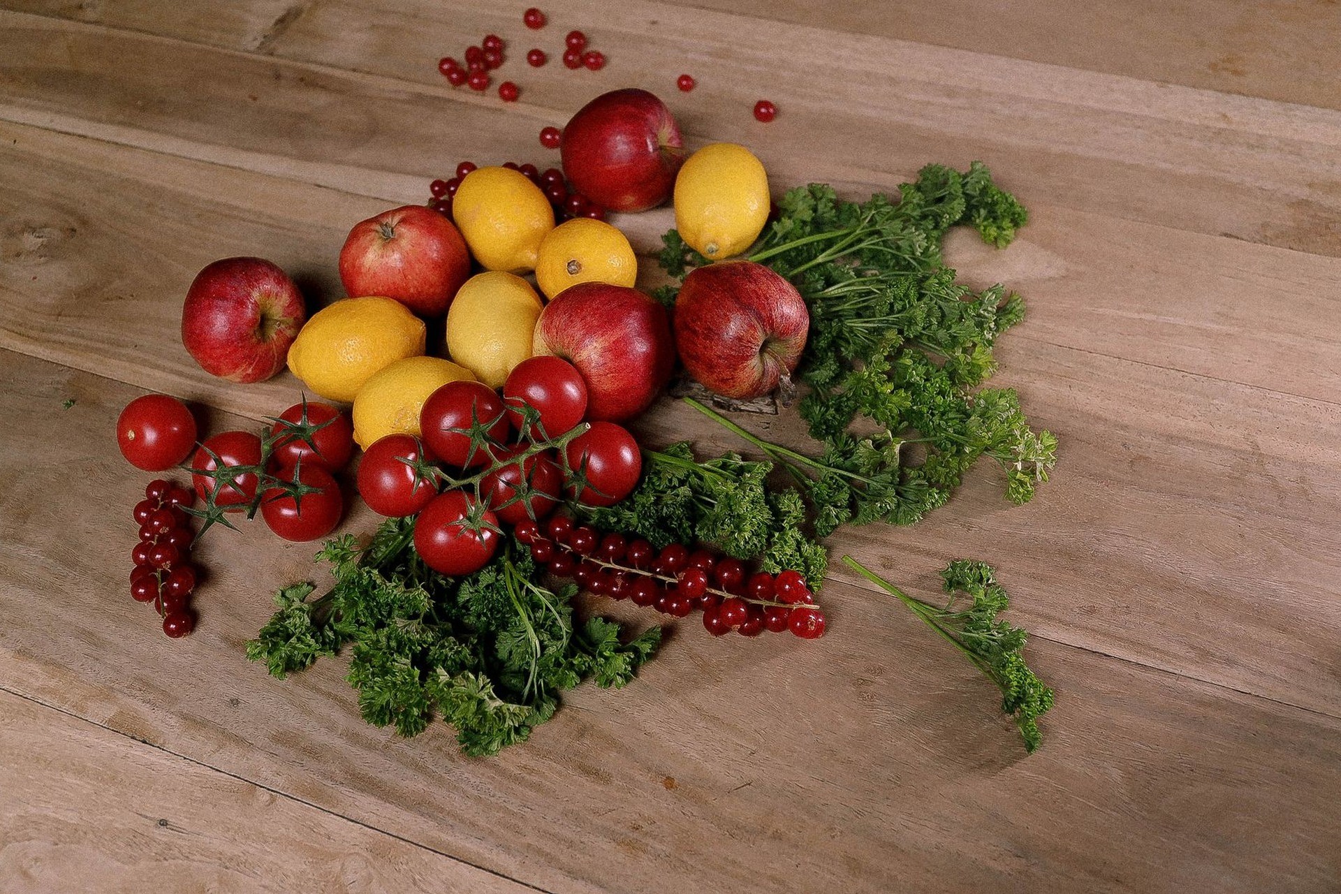 Manzanas, limones, tomates cherry y hierbas frescas sobre una mesa de madera