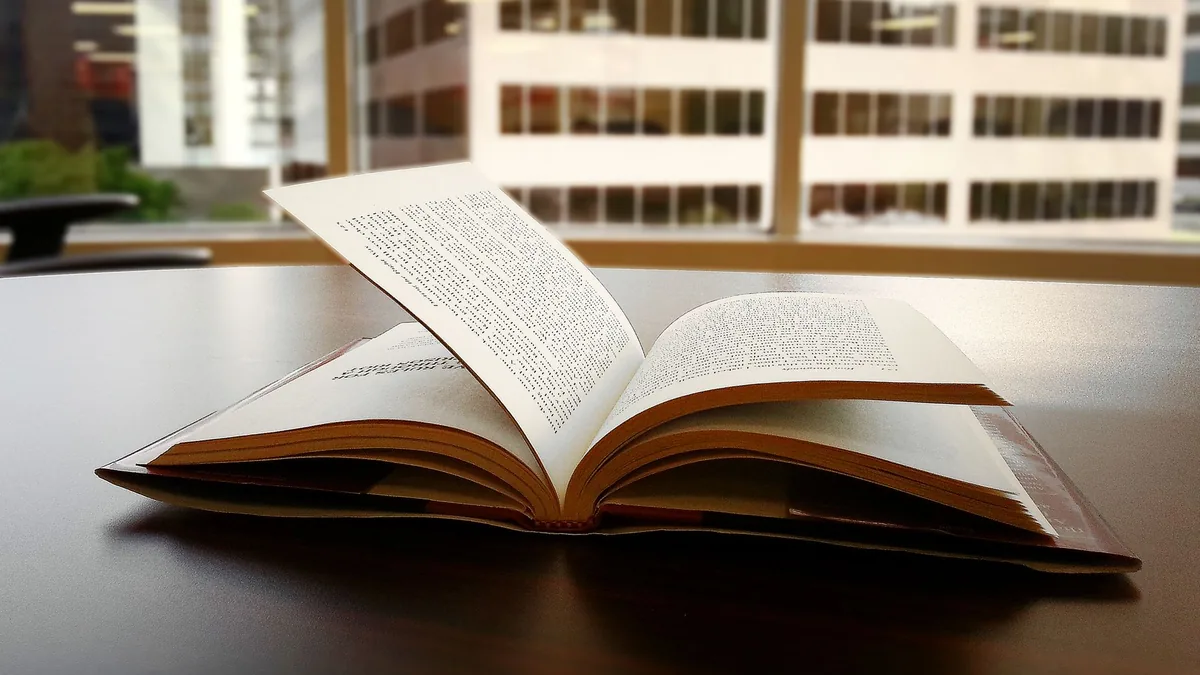 Un libro abierto se encuentra sobre un escritorio en una oficina con vista al horizonte de la ciudad a través de grandes