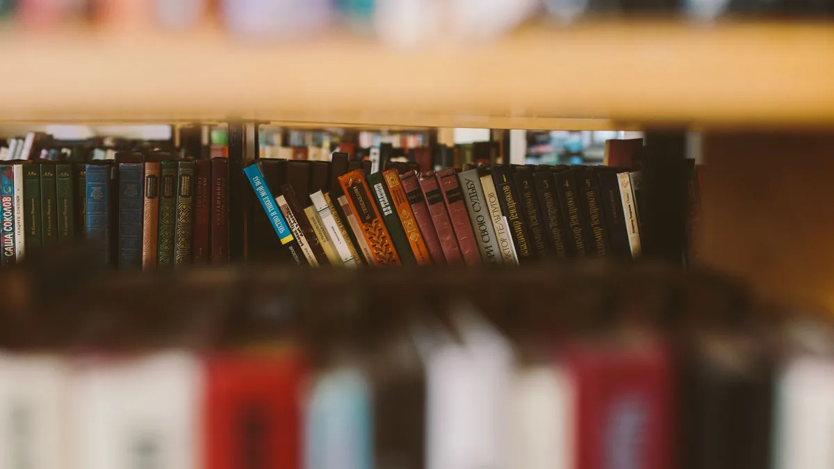 Primer plano de una variedad de libros en una estantería de madera en un ambiente de biblioteca.